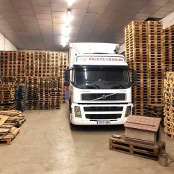 Vista interior de nave con palets almacenados y camión de empresa en primer plano