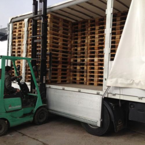 Trabajador con camión grúa descargando palets de camión